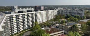 Panoramaaufnahme eines großen Wohnkomplexes mit mehreren Stockwerken und umliegenden Grünflächen und Parkplätzen.