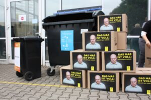 Kartons mit dem Aufdruck "Das Maß ist voll" vor einer Blauen Tonne