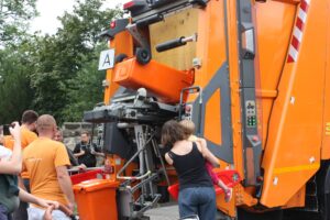 Orangefarbenes Müllfahrzeug kippt Tonne