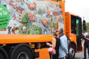 Frau und Mann schauen ein Wimmelbild auf einem Müllfahrzeug an