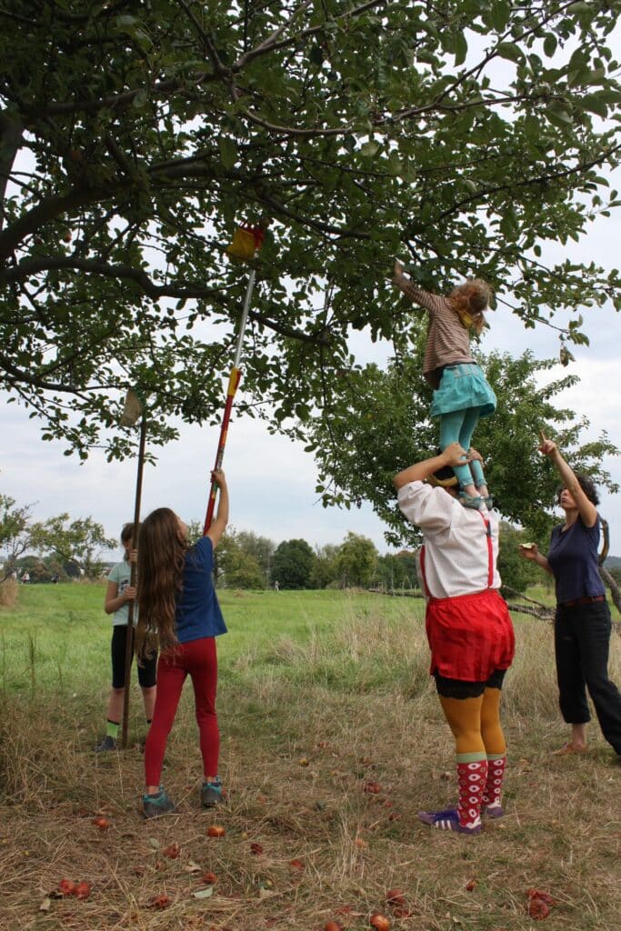 Mädchen steht auf Clown und greift nach Äpfeln
