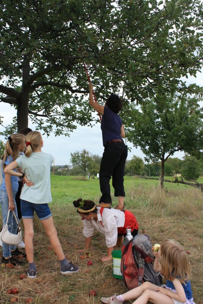 Frau steht auf Clown an einem Baum und Kinder schauen zu