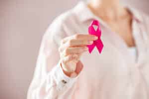 Nahaufnahme einer Frau, die eine rosa Schleife zur Aufklärung über Brustkrebs hält. Detail der weiblichen Hand hält rosa Bewusstsein Band. Junge Frau, die das Leben mit Brusttumor bei Frauen unterstützt.