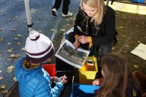 Frau zeigt Kindern ein Infoblatt zum Thema Abfall