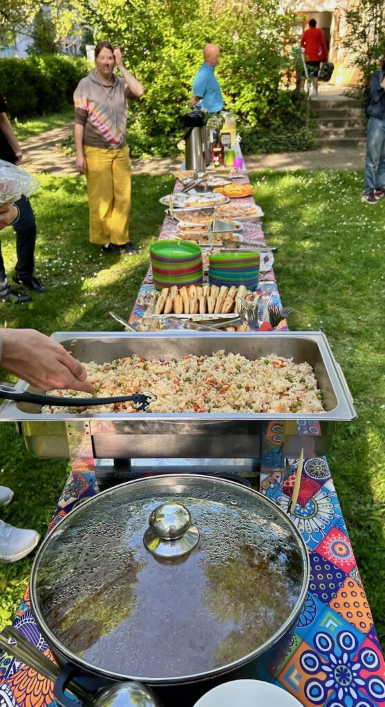 eine lange Tafel voller Speisen im Garten des Johannstädter Kulturtreffs; im Vordergrund eine große Metallschale voller Reis mit Gemüse