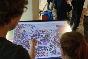 Zwei Personen betrachten einen Ausschnitt eines Stadtplans auf einem Monitor.