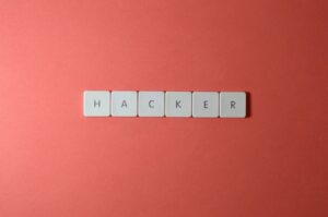 Nahaufnahme des Wortes „HACKER“, das aus Buchstabenfliesen auf rotem Hintergrund besteht und die Cybersicherheit betont.