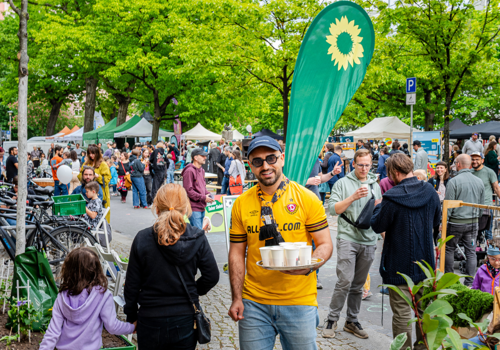 Mann mit Cappi und Sonnenbrille hält auf einem Fest ein Tablett mit Bechern in der Hand