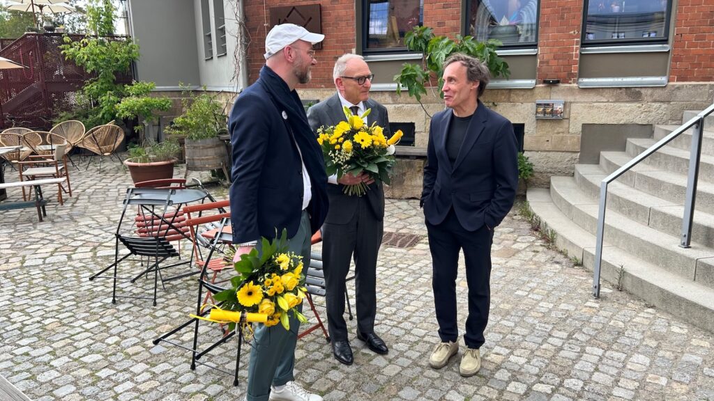 drei Herren, zwei mit Blumensträßen