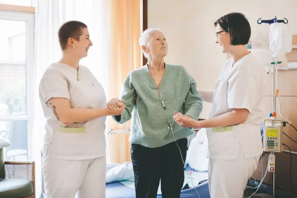 Zwei Pflegerinnen stützen einen Patienten beim Laufen.