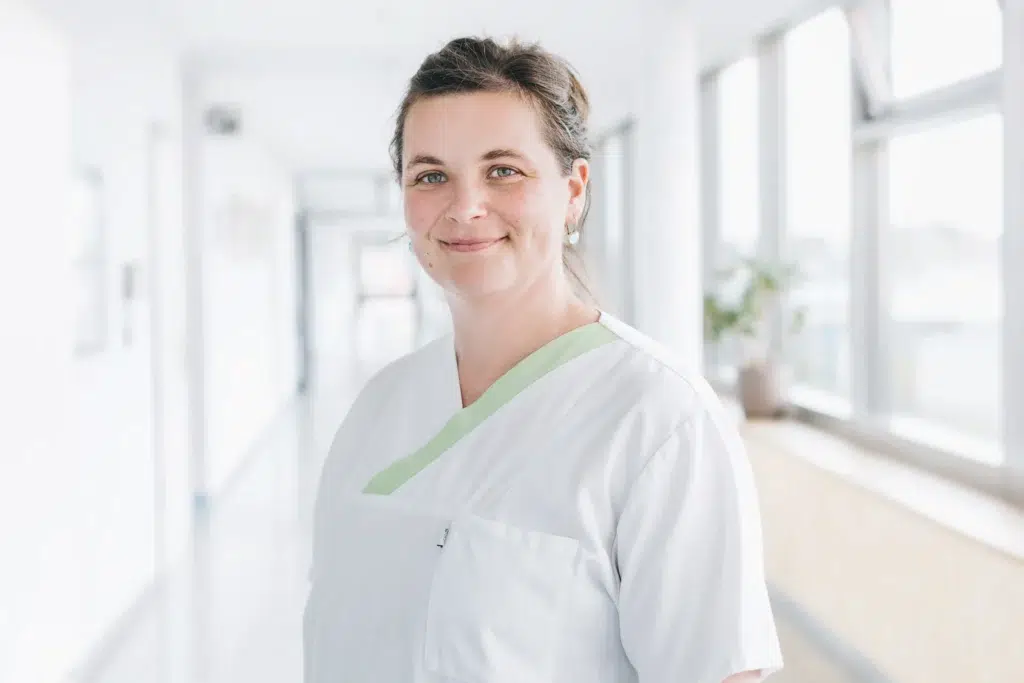 Ein junge Frau, brünett, mit freundlichem Gesicht und in weißer Berufskleidung.
