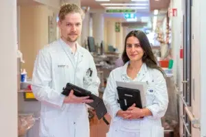 Ein Mann und eine Frau, beide in weißen Kitteln, stehen in einem Krankenhausflur.