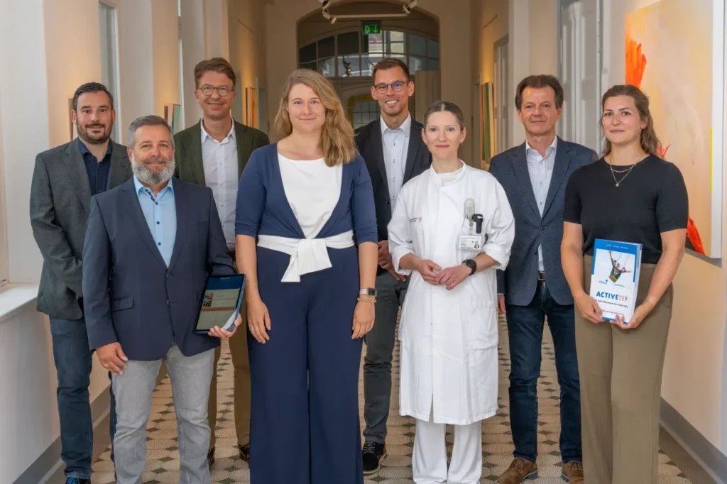 Gruppenbild von acht Personen, drei Frauen und fünf Männer, in einem Gebäudeflur.